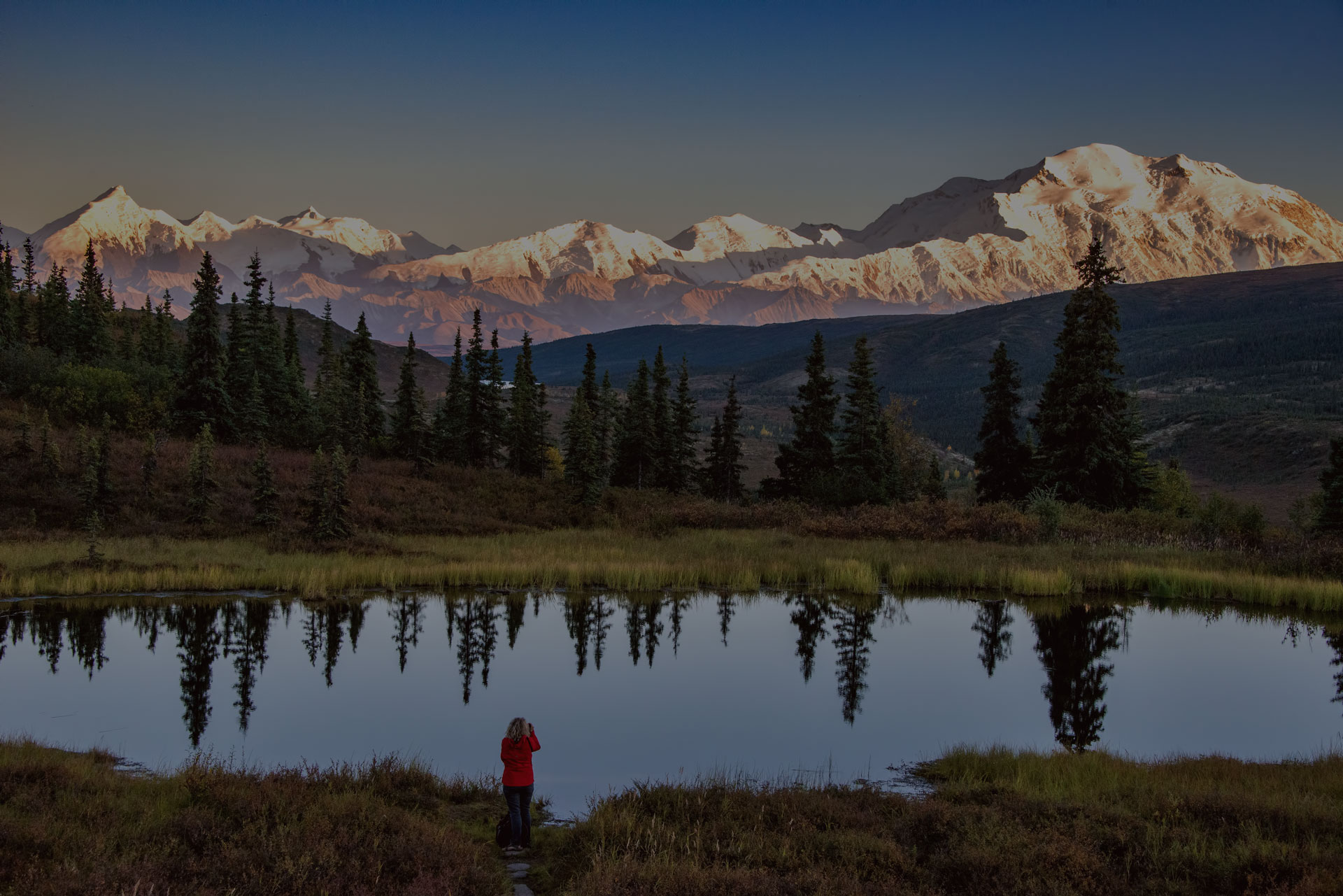 view of alaska's mount denali looms over calm pond at sunset